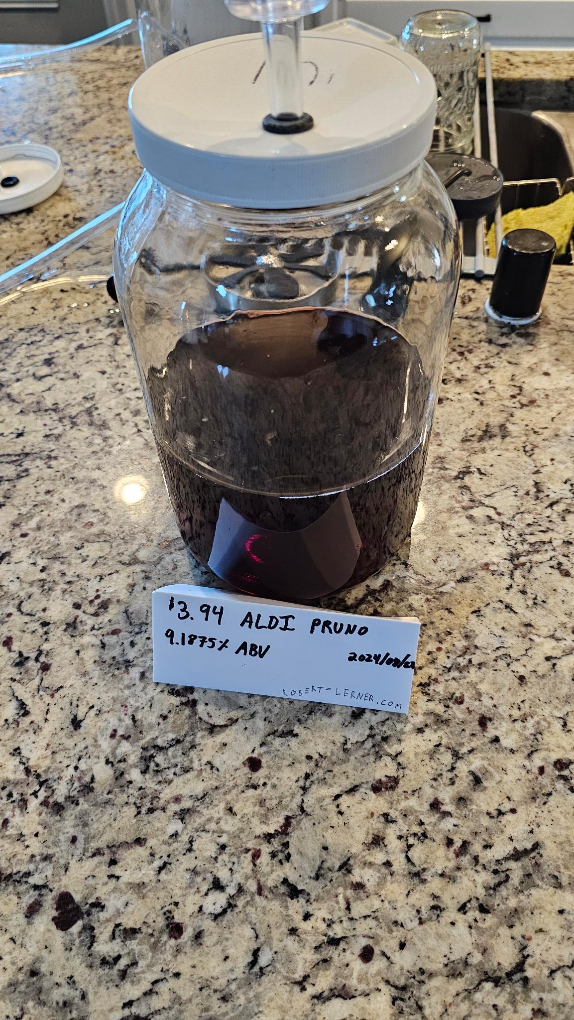 A one gallon glass fermenter sporting prison wine and a cylinder style airlock.